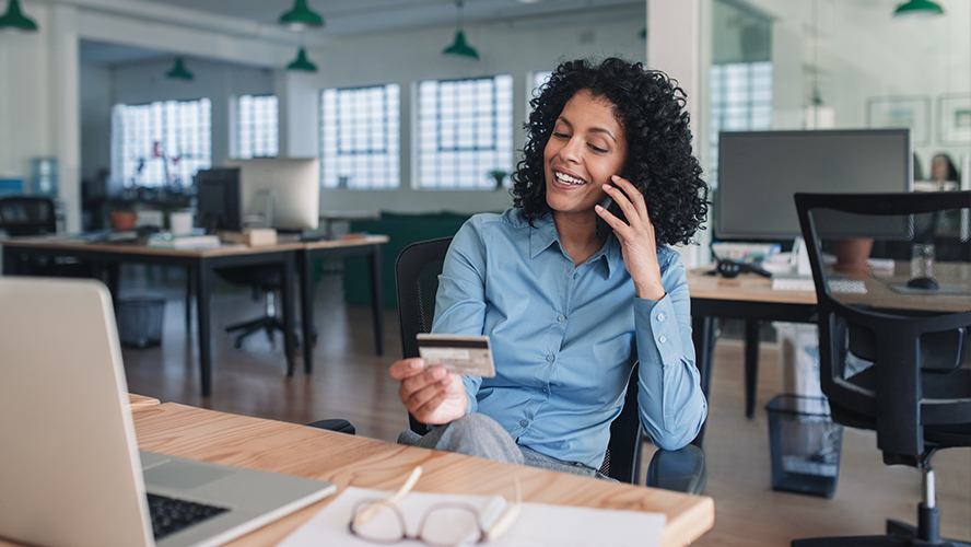 Woman at desk on the phone and holding credit card.