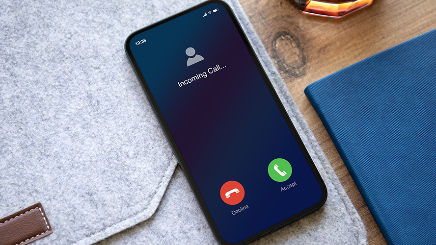 Image of a cell phone laying on a desk with an incoming call on the screen.