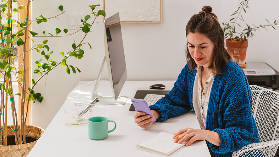 A woman sitting at a desk, looking at her phone.