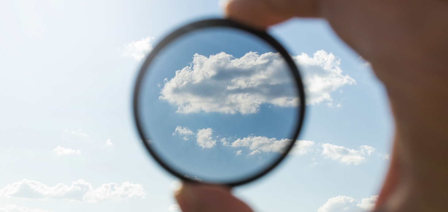 A hand holding up a lens to show a clearer image of a cloudy blue sky.