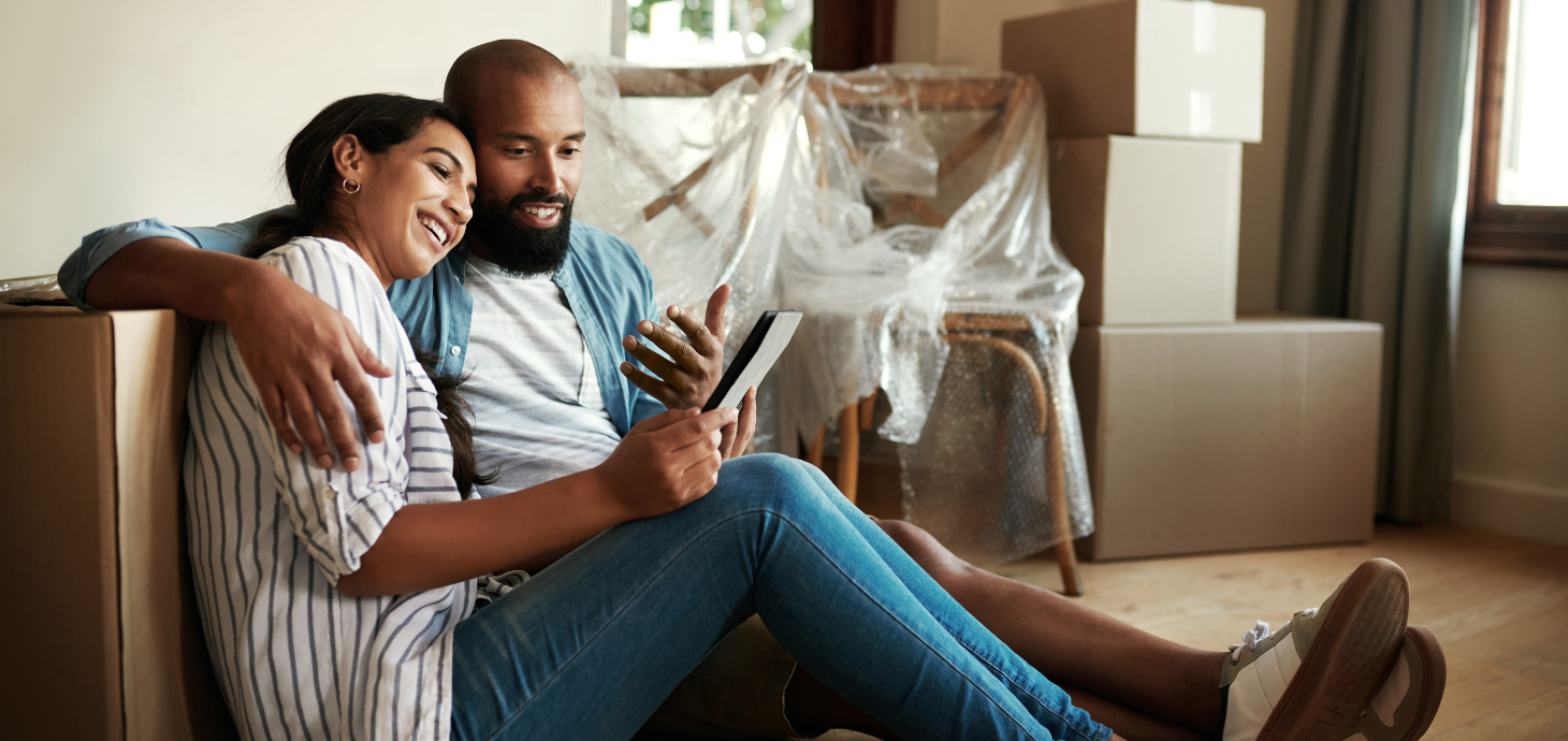 Two homeowners sitting on the floor surrounded by moving boxes.