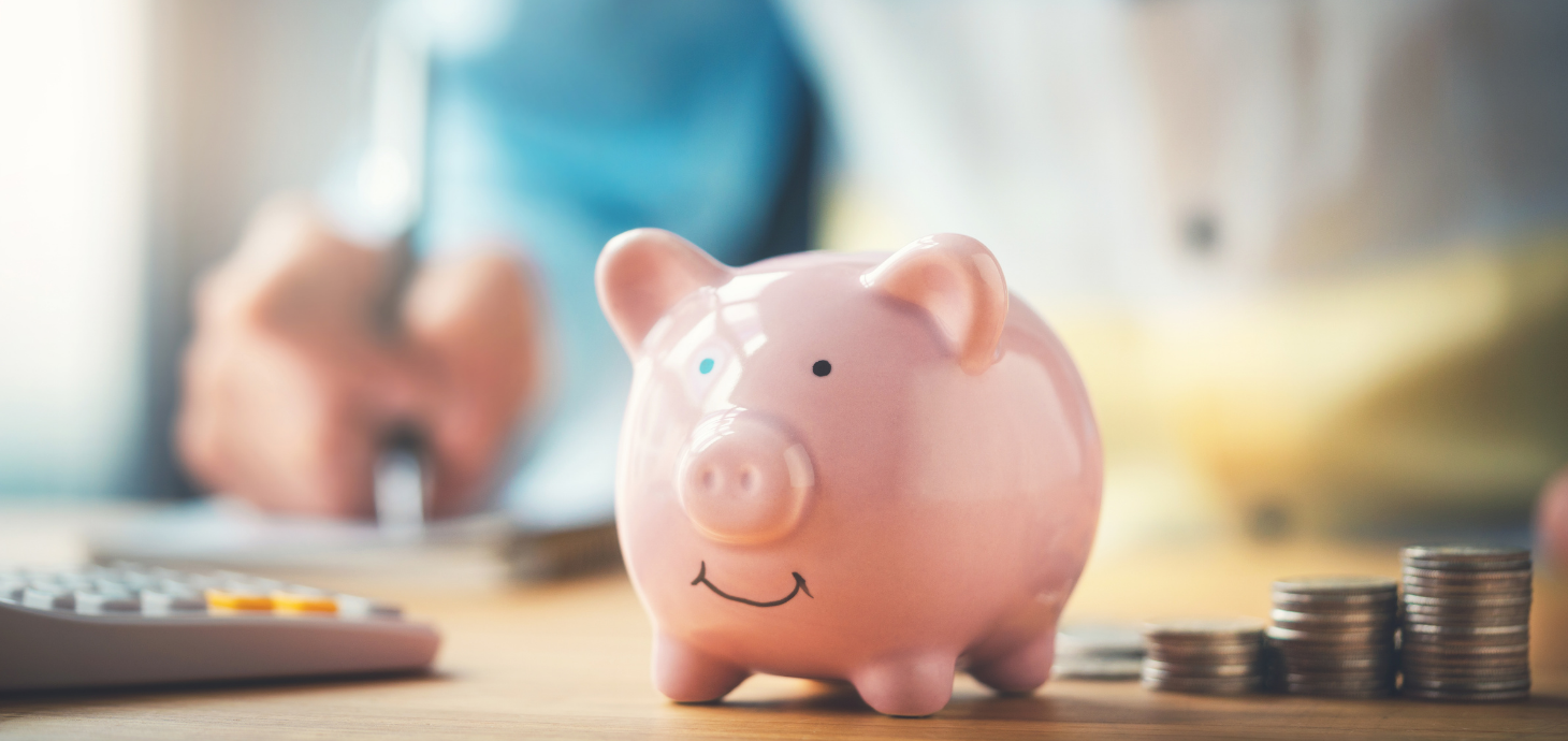 PIggy bank on table next to calculator and piles of coins.