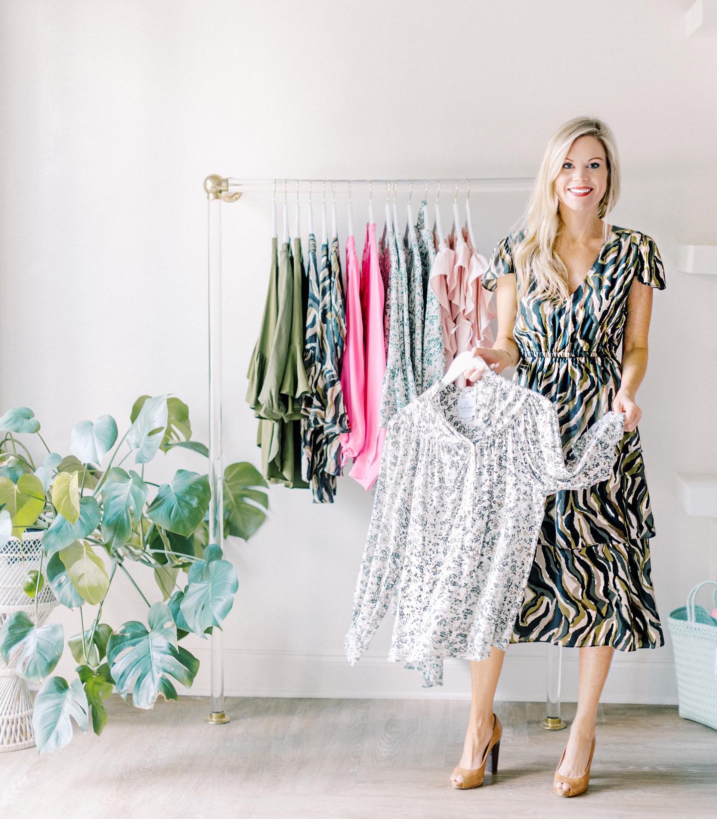 Woman standing next to a rack of clothes holding a shirt on a hanger.